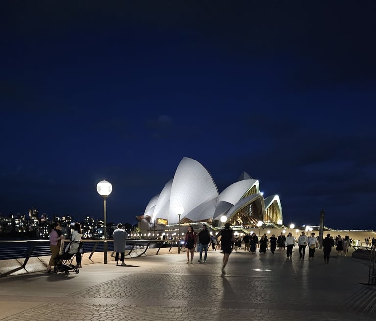 Night view of the Sydney Opera House illuminated with crowds walking along the harbor boardwalk.