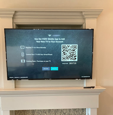 Above-fireplace mounted VIZIO smart TV displaying a setup screen with a QR code for the mobile app.
