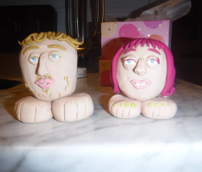 Handmade clay figurines of a man and woman with large feet sitting on a marble counter.