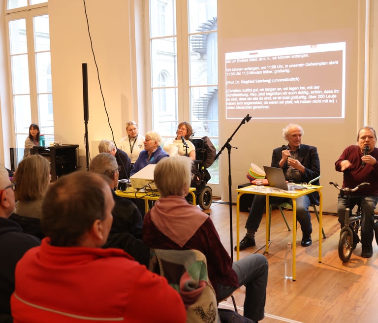 Zwei Menschen mit Behinderung sprechen vor einer Gruppe von Menschen
