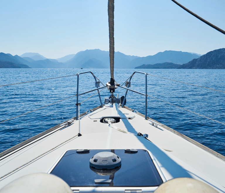 Desde la proa de un velero, paisaje de montañas al fondo y mar en calma