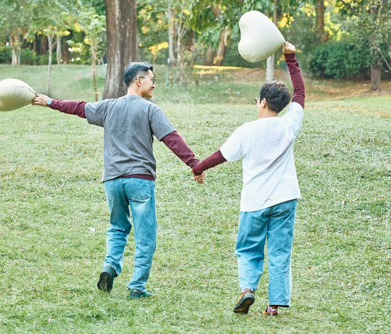 A happy young couple holding hands and carrying heart-shaped balloons in a lush green park.