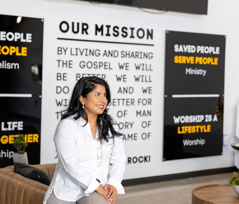 Melissa, founder of Bee the Light Designs sitting in from of her designed church mission wall