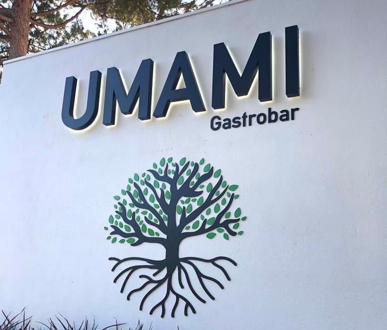Umami Gastrobar signage on a white wall with a decorative tree logo and outdoor landscaping.