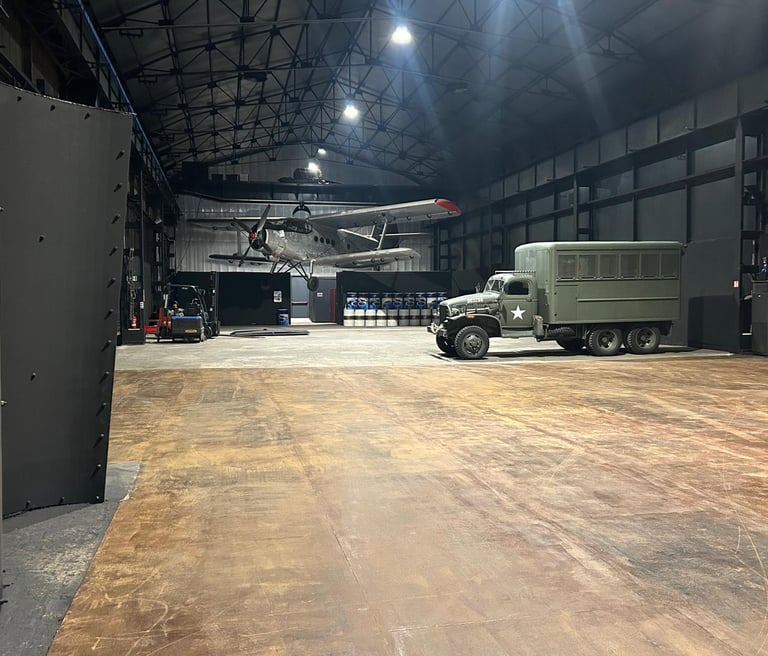 Vintage military airplane and army truck inside a large industrial hangar warehouse.