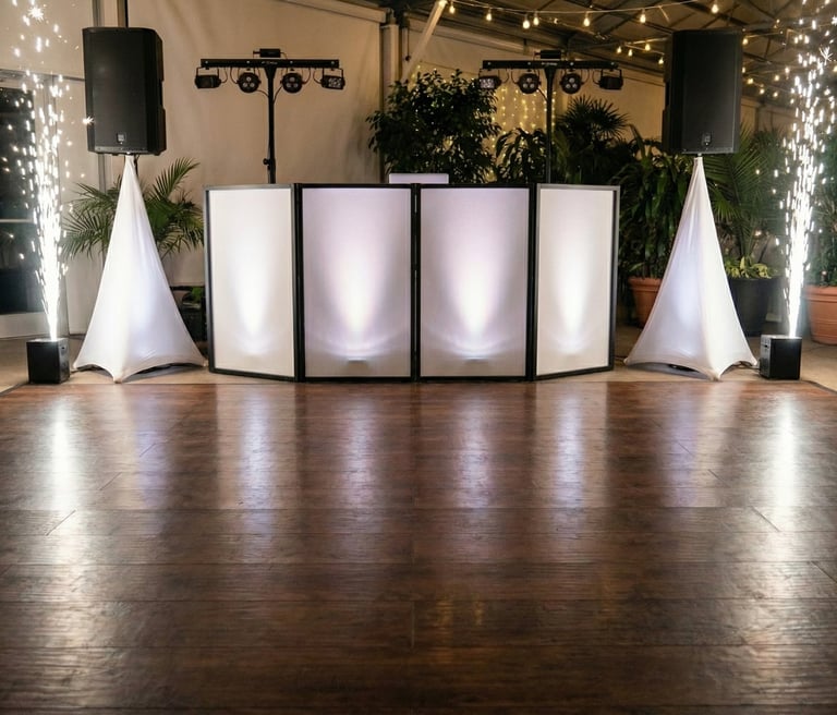 Professional wedding DJ booth setup with white facade, speakers, and cold sparklers on a wood dance floor.