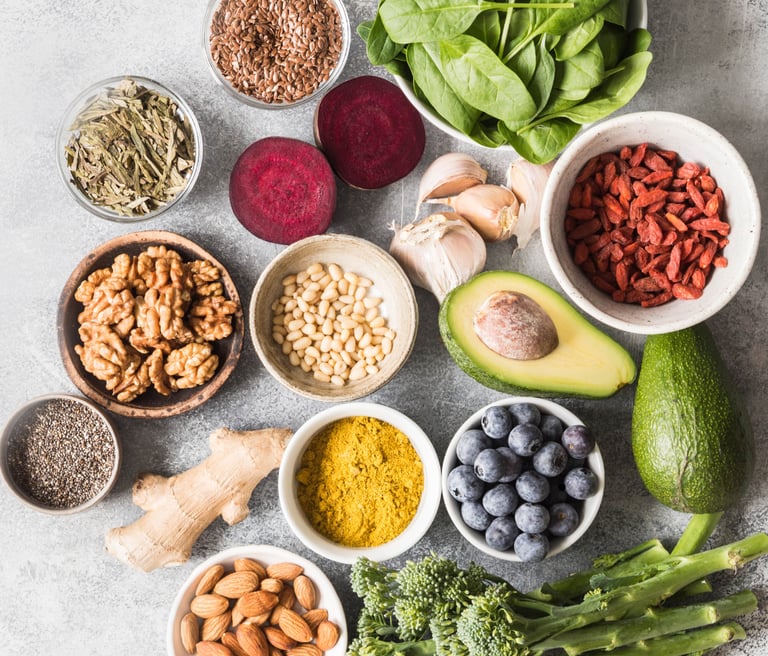 Flat lay of healthy superfoods including avocado, blueberries, walnuts, almonds, and leafy greens for a nutritious diet.