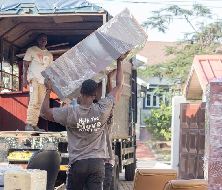Two movers, one inside an open-back truck and another outside, lift large wrapped boxes and panels d