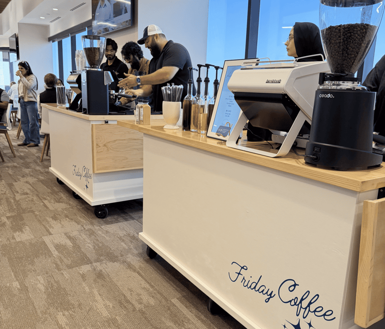 Professional baristas preparing espresso drinks at a Friday Coffee mobile catering cart in a modern office lobby.