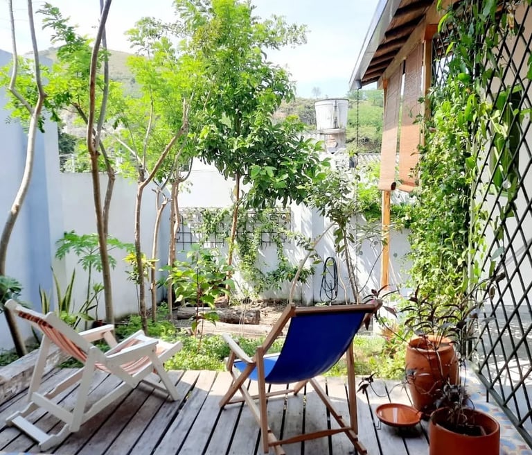 Two folding wooden lounge chairs on a rustic garden deck surrounded by lush green trees and plants.
