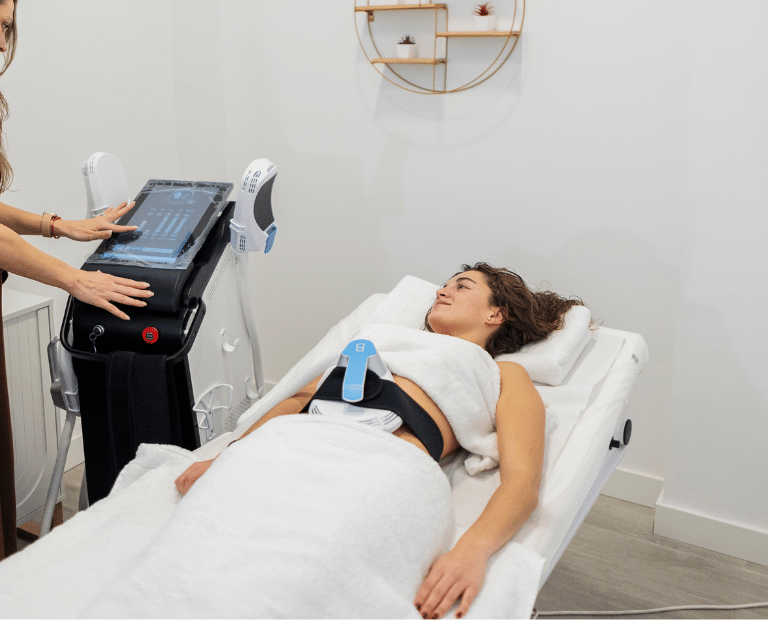 woman sitting on clinic bed with emsculpt machine on stomach
