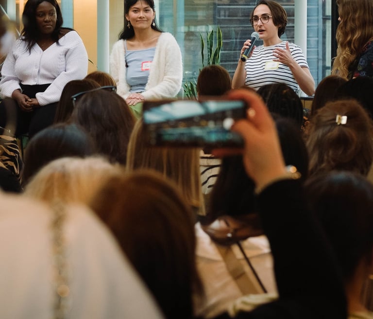 Photo of Micha in a stripy t-shirt holding a microphone and speaking to an audience