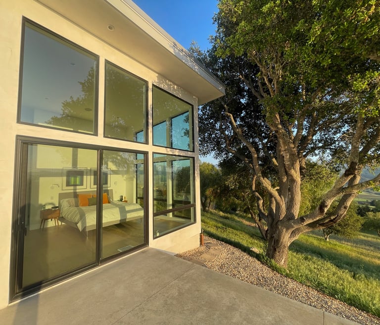 Modern luxury bedroom with floor-to-ceiling glass windows and sliding doors overlooking a lush hillside.