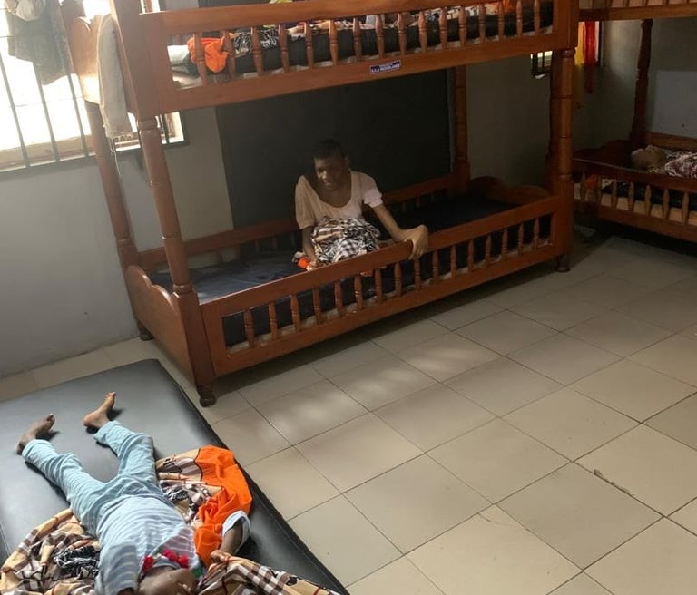 A shared bedroom with wooden bunk beds and a child lying on a floor mattress.