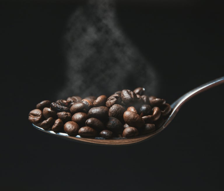 A spoon with freshly roasted coffee beans with fresh smoke visible