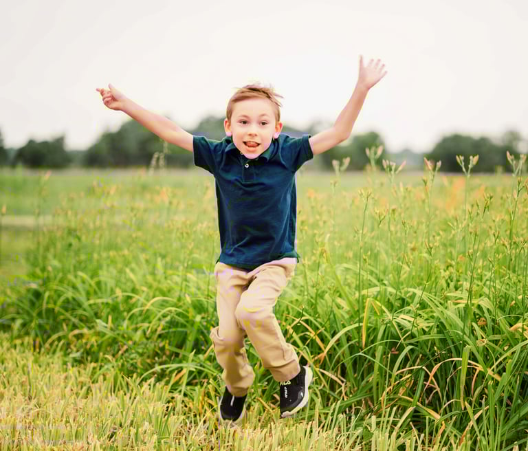 a young boy jumping in the grass with his hands up