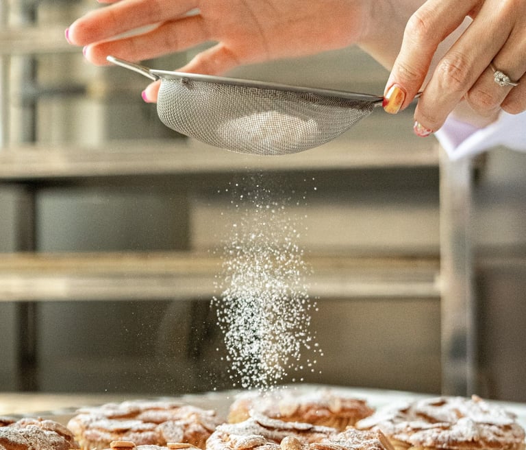Un chef pastelero espolvoreando azúcar glass sobre tartaletas recién horneadas