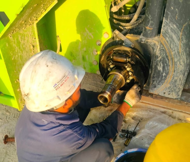 A mechanic in a white hard hat performs heavy equipment brake repair on a construction vehicle axle.