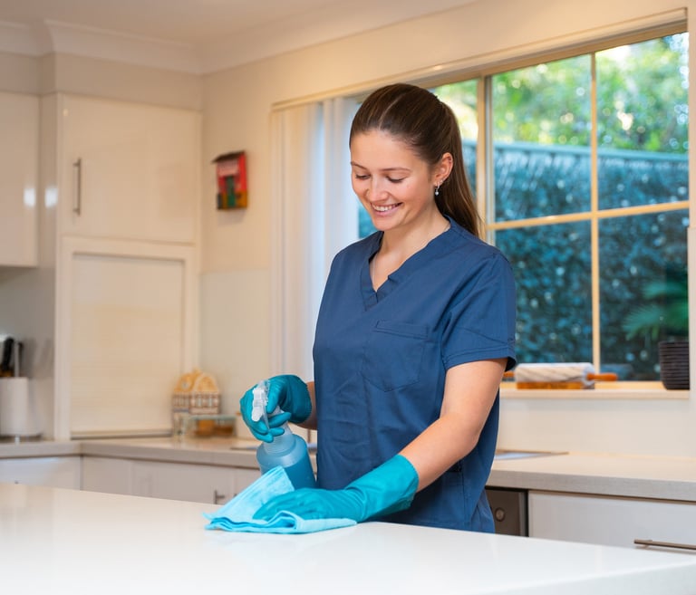 a woman in scrubs and gloves is smiling and cleaning a kitchen counter top