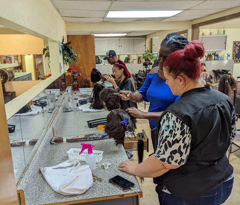 Students and instructors practice hair styling and cutting techniques on mannequin heads in a cosmetology school salon class.