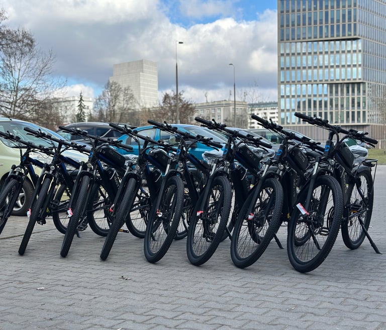 A row of black electric mountain bikes parked on a city street near modern office buildings.