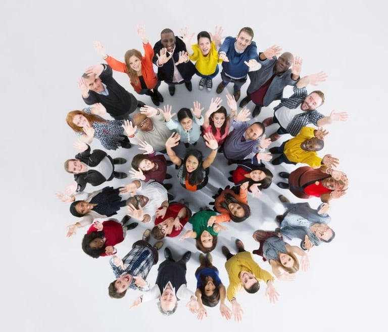 A diverse group of smiling people standing in a circle looking up and waving at the camera.
