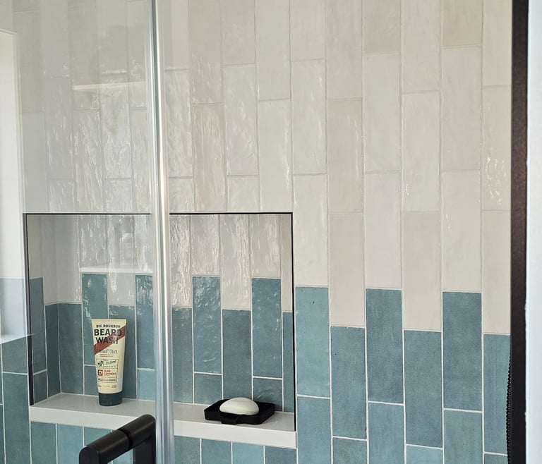 Modern walk-in shower with vertical blue and white subway tiles, glass doors, and black hardware.