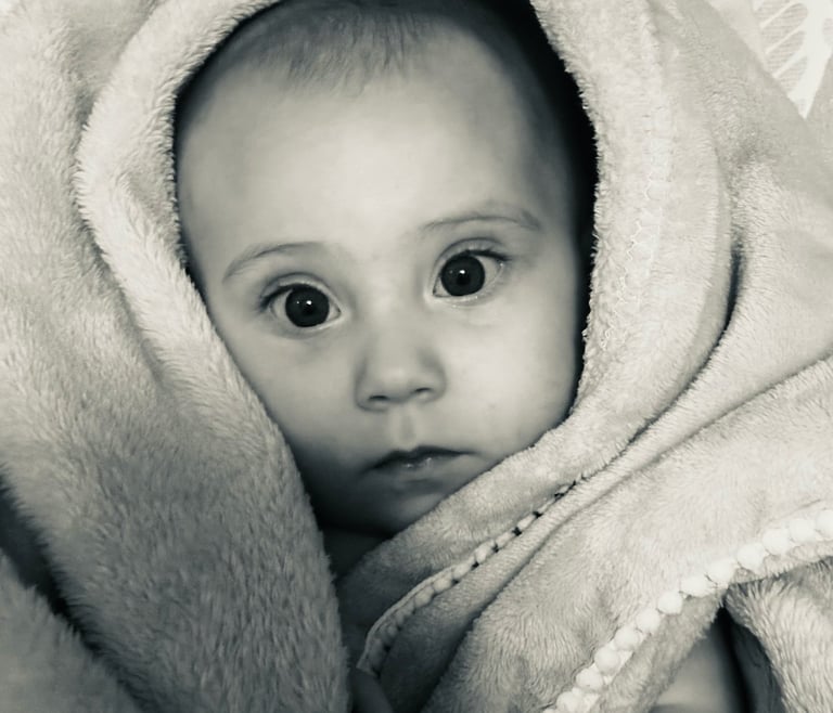 Black and white photo of a baby girl wrapped in a soft blanket, gazing at the camera with wide eyes.