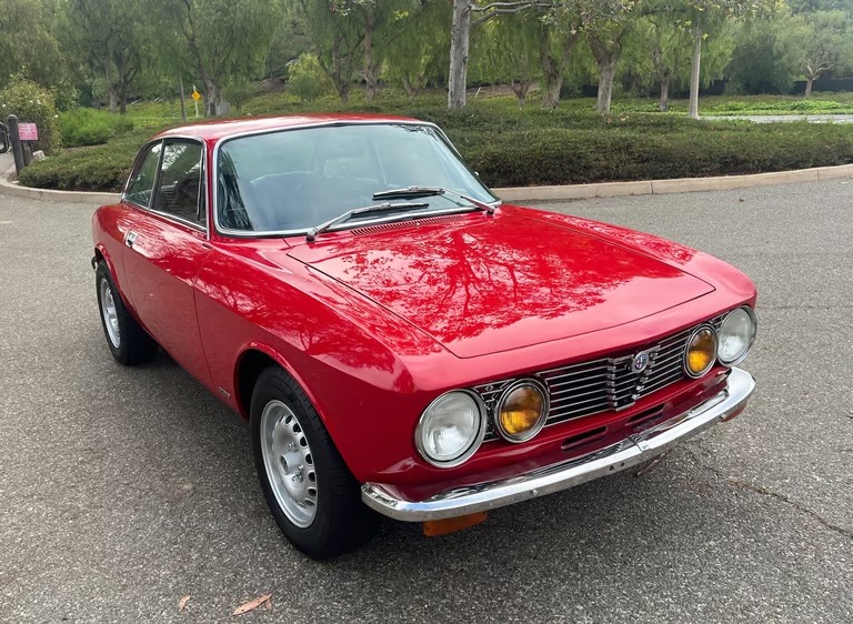 A photo of a red 1974 Alfa Romeo GTV 2000 in a park setting.