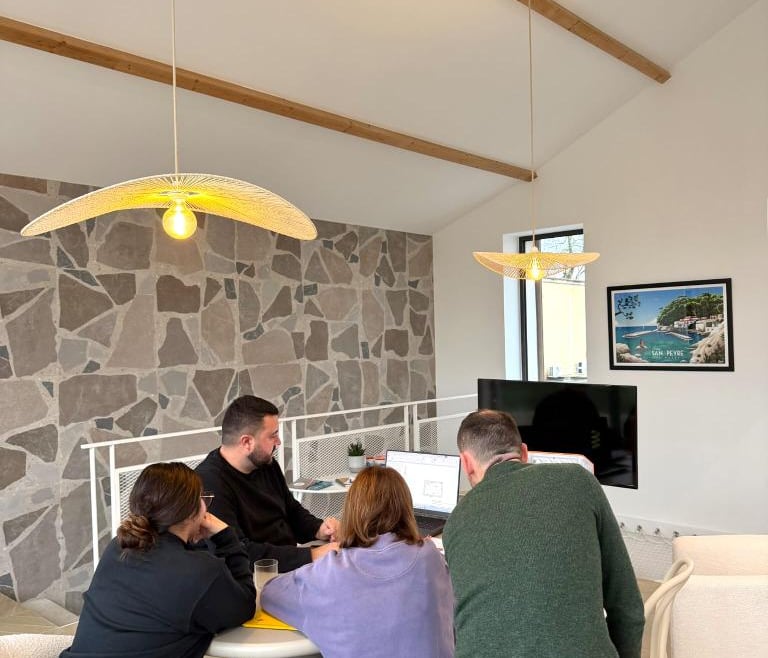 A team of young professionals collaborates at a table in a modern office with stone walls and pendant lighting.
