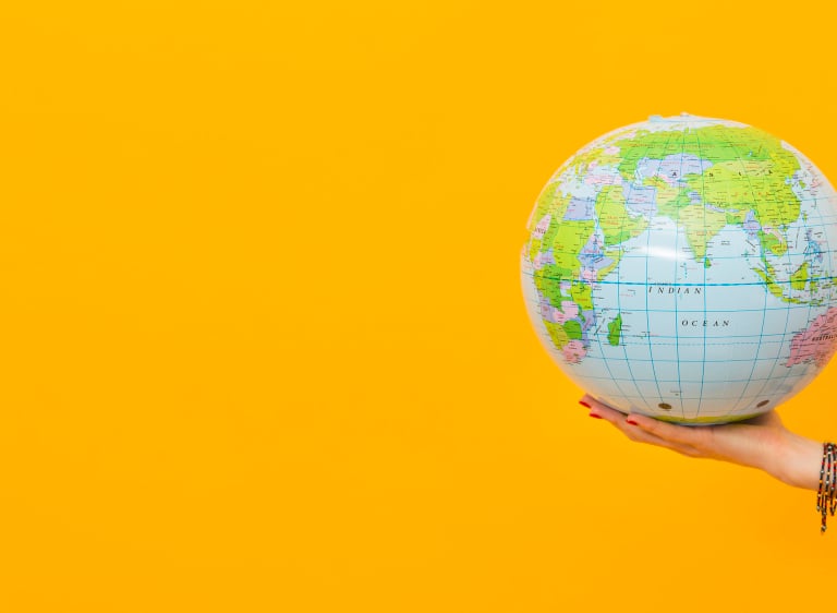 A person holding an inflatable world globe against a vibrant yellow background for global travel concepts.