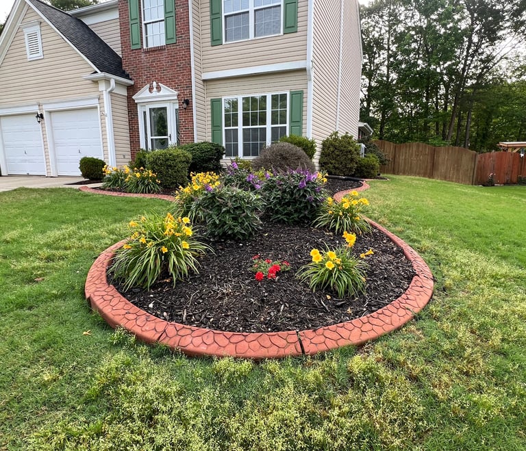 View of flower bed with red border with flowers installed where tree was removed.