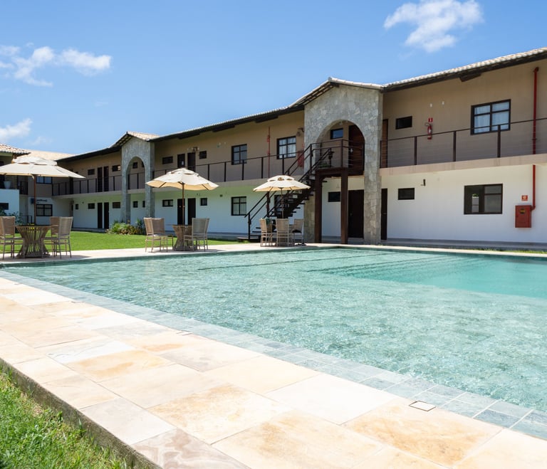Luxury resort swimming pool with crystal clear water, patio umbrellas, and stone arch architecture.