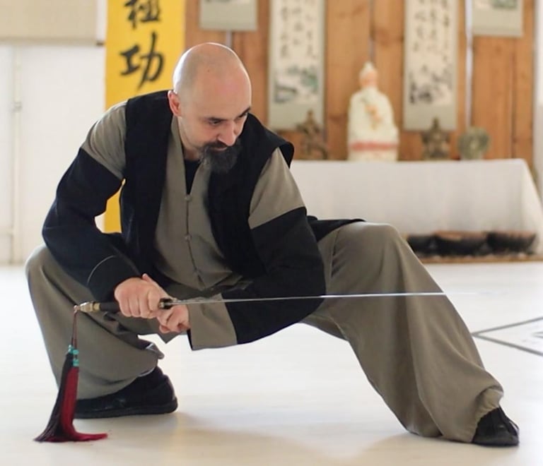 Ismet Himmet demonstrating a low Wudang sword stance (Jian) during indoor training with altar behind.