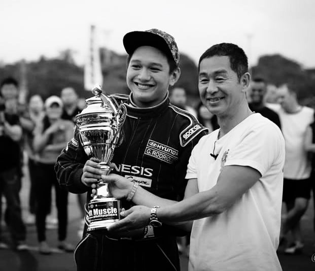 Keiichi Tsuchiya handing a trophy to a man in front of a crowd