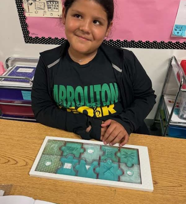 girl sits with a completed Braille Skills Puzzle in front of her, a look of pride on her face