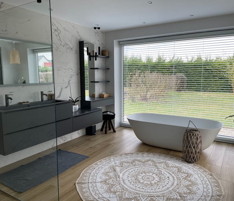 Modern bathroom with marble walls, double vanity, and a freestanding oval bathtub by a large window.