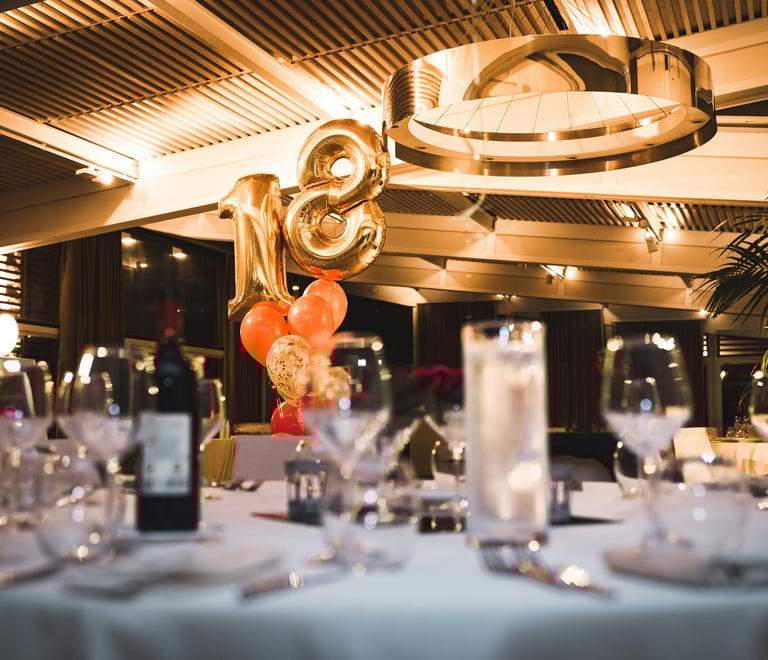 Elegant 18th birthday party table setting with gold number balloons and wine glasses.