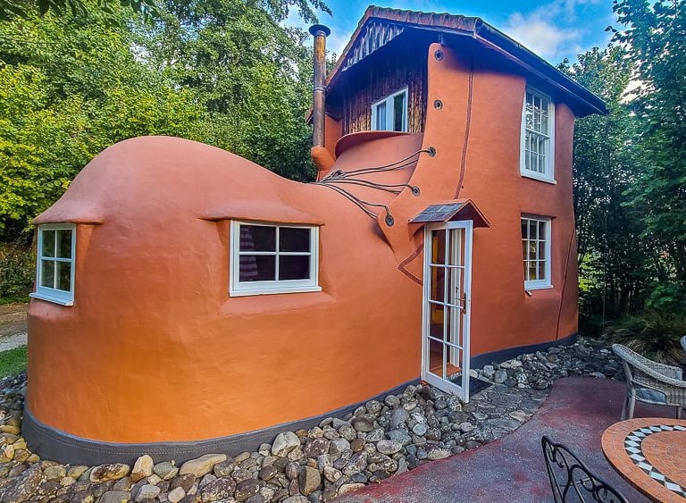 A whimsical giant orange shoe house cottage with windows and a door nestled in a lush green forest.