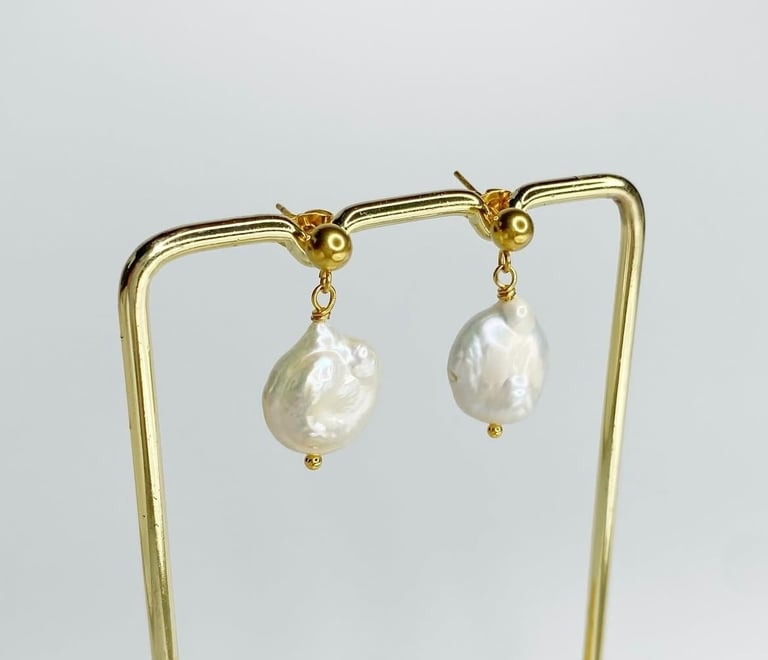 Elegantes pendientes colgantes de perlas barrocas doradas exhibidos en un expositor de joyas.