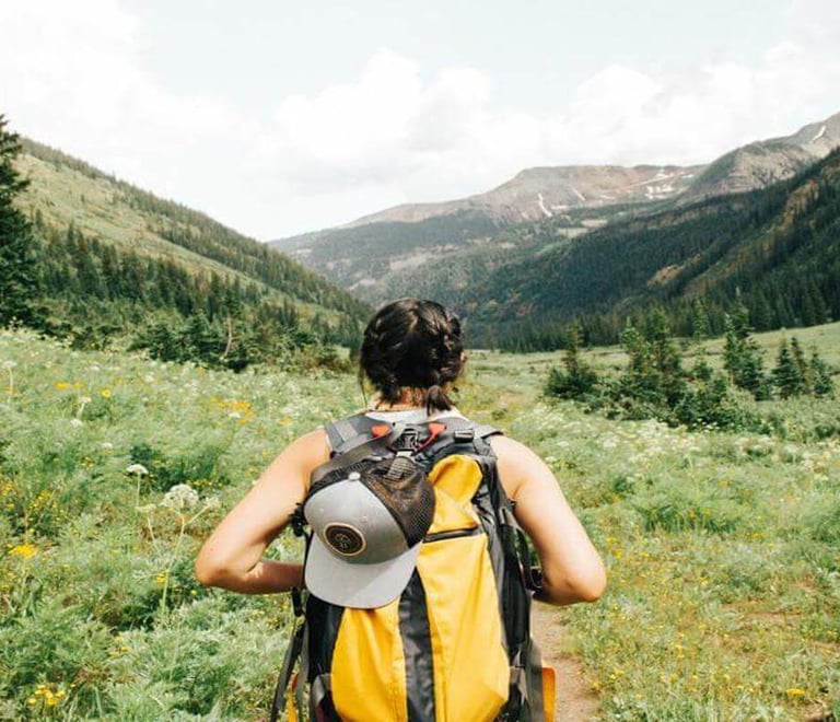 Person hiking through a green mountain valley with a backpack.
