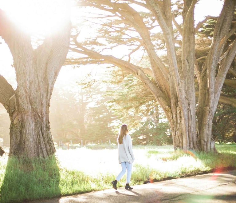 a woman walking down a path with trees in the background
