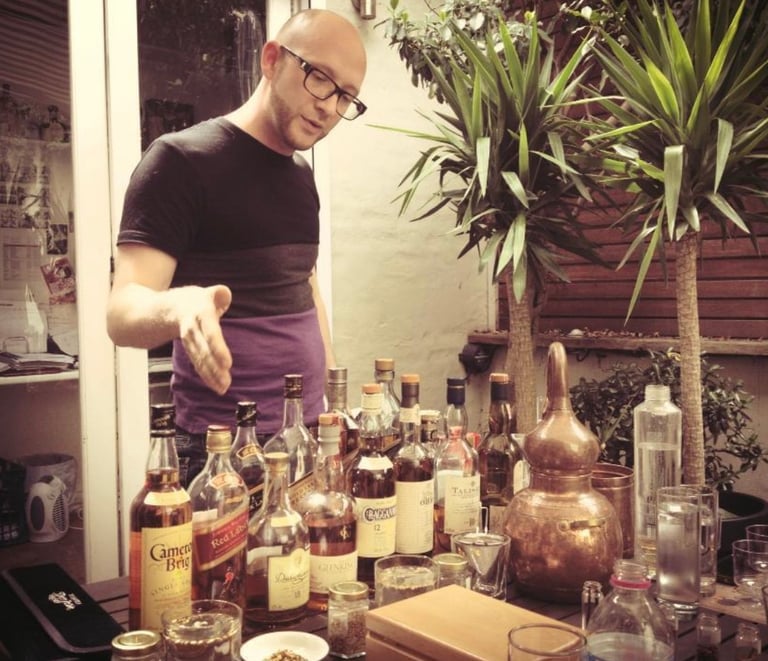 a man in a black shirt is standing in front of a table with bottles of whisky