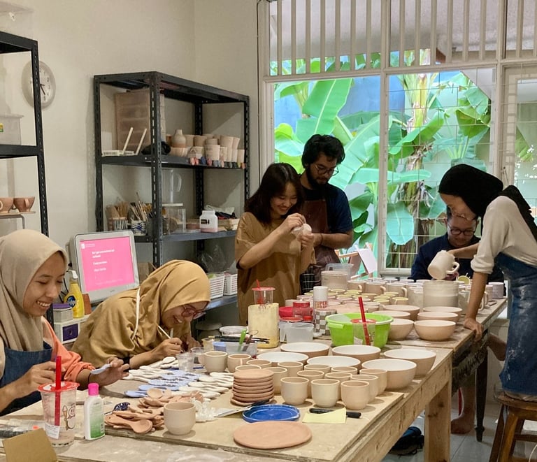 a group of people laughing together while sitting at a table making handmade pottery
