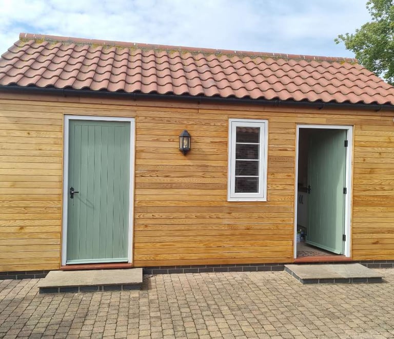 Exterior of a small building, with walls covered in wood-panelling and doors painted green..