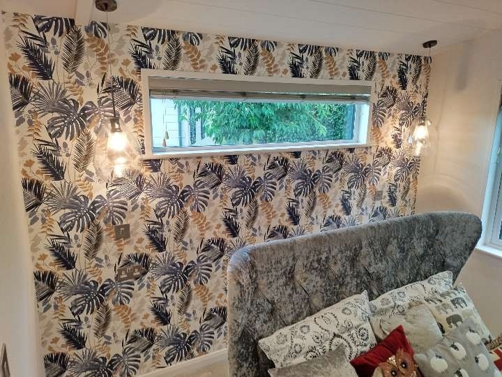 Cosy living room, with a white, fern-style feature wall, grey sofa, and thin upper window.
