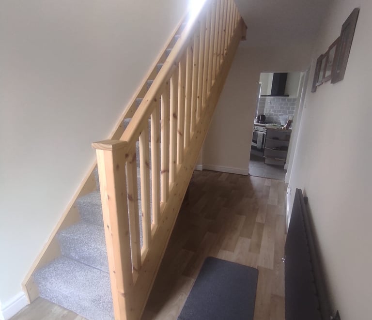 Modern entrance hallway, with painted white walls/ceiling, light-wooden banister, and wood flooring.