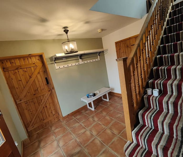 Rustic entrance hallway, with a white wall/ceiling, a pale-green wall, and red-slab flooring.