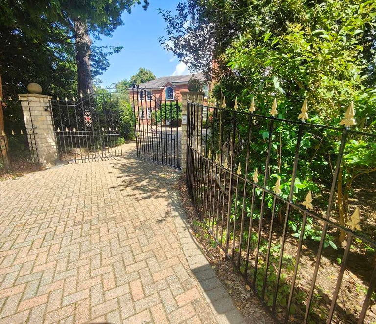 Exterior brick driveway, with painted black fencing and gate, adorned with gold arrowheads.