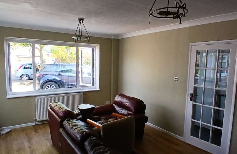 A furnished sitting room, with light-brown walls, a wooden floor, and white detailing.
